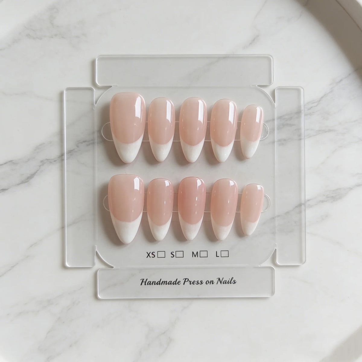A set of pink handmade press-on nails in a French almond style displayed on a clear plastic tray.