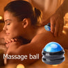A hand is massaging a glowing blue massage ball on the shoulder of a person in a warm, dimly lit setting.