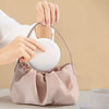 A hand is placing a white LED makeup mirror into a light pink cosmetic bag.