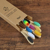 A box containing a set of ten natural bamboo toothbrushes in various colors, resting on a wooden surface.