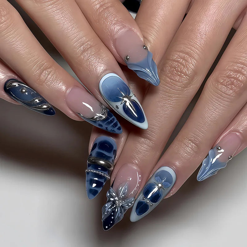 A close-up of elegant almond press-on nails featuring blue and white floral and butterfly designs.