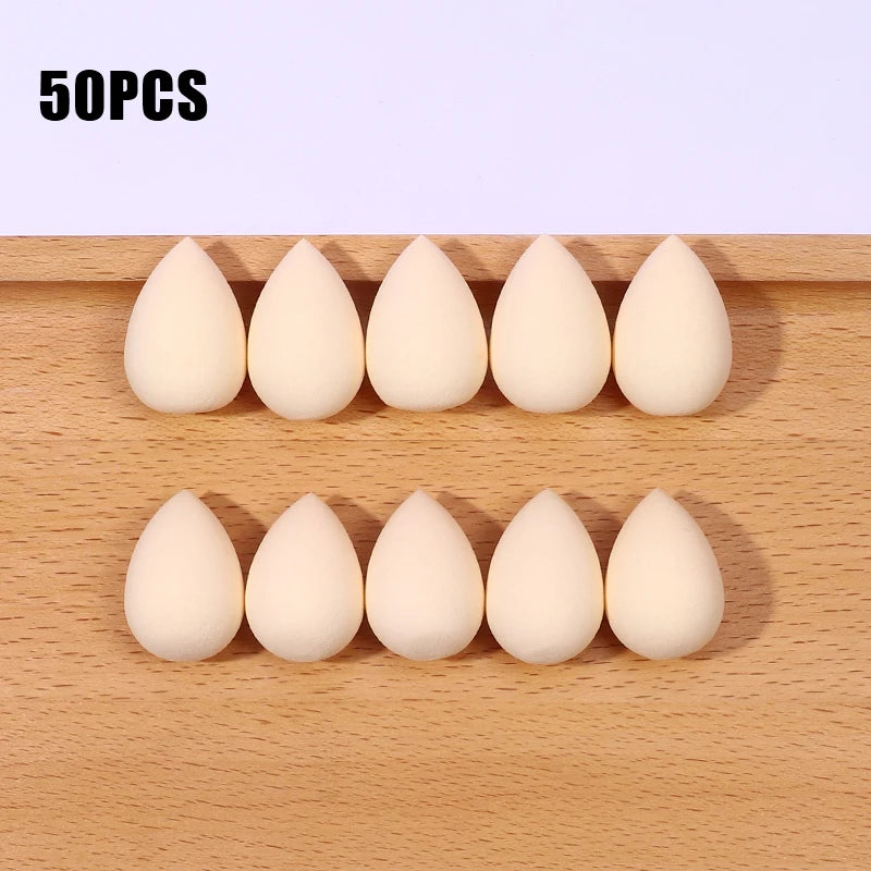 Fifty white makeup sponge puffs arranged in two rows on a wooden surface.