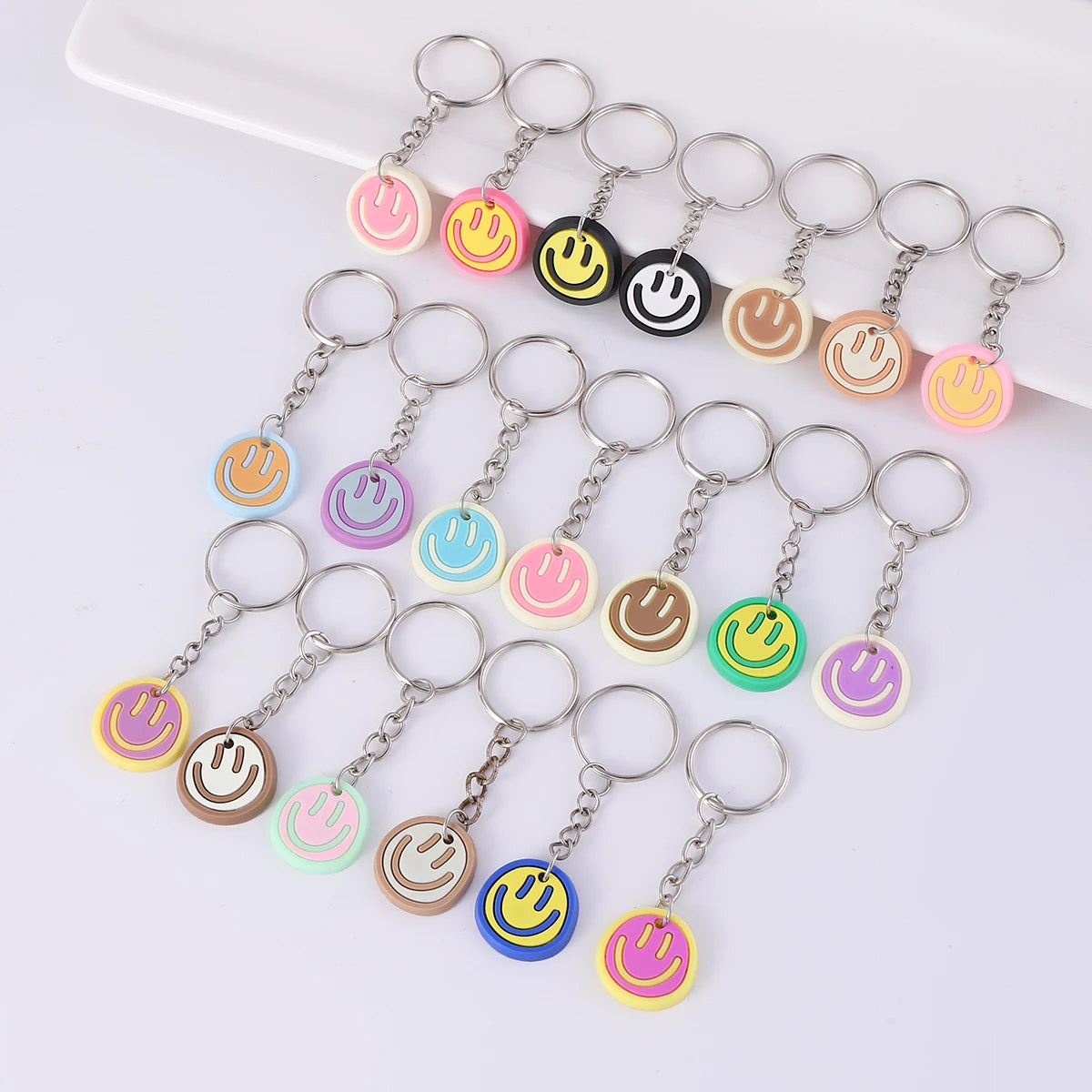A set of 20 colorful cartoon smile face keychains hanging from metal rings on a white surface.