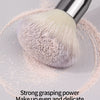 A silver face powder brush with soft pink powder is shown on a light gray surface.