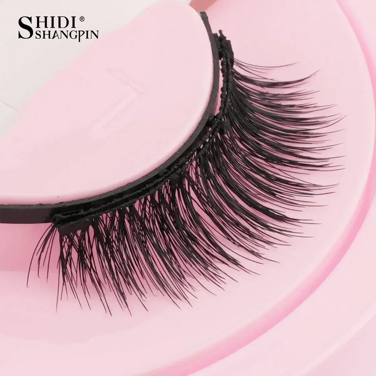 Gros plan d'une mèche de faux cils noirs présentée sur un outil cosmétique rose.