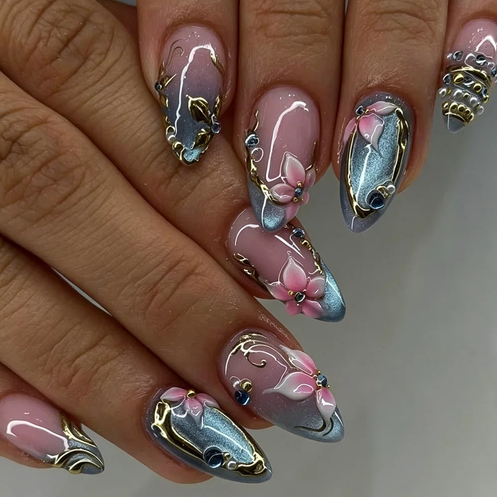 A close-up of a hand displaying 24-piece almond press-on nails featuring delicate silver and pink floral and butterfly design