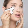 A woman is using a stainless steel gua sha massager on her face for skincare.
