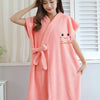 A woman wearing a coral pink microfiber bathrobe with a smile design standing indoors.