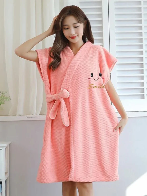 A woman wearing a coral pink microfiber bathrobe with a smile design standing indoors.