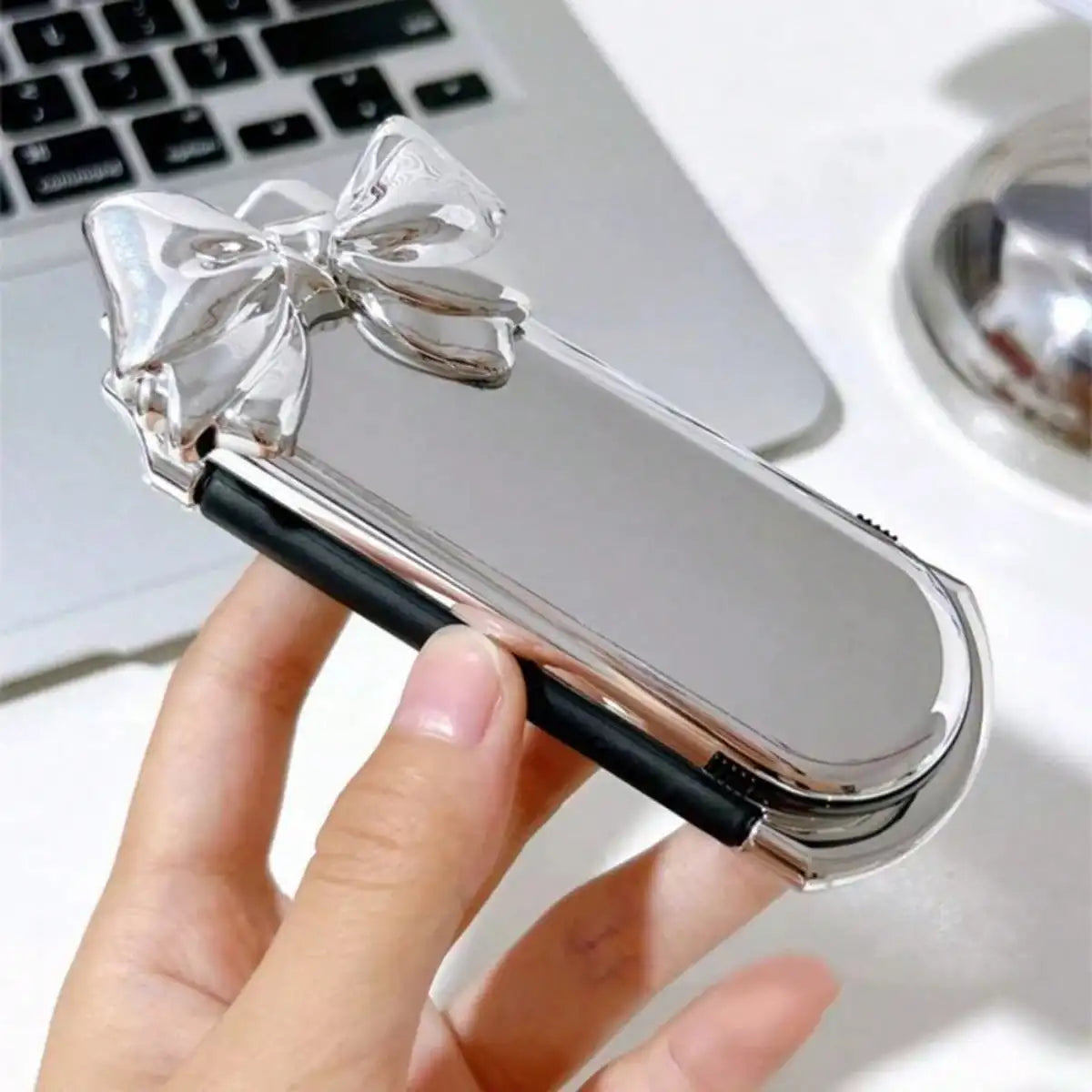 A hand holds a silver portable compact comb with an airbag and mirror on a white surface.