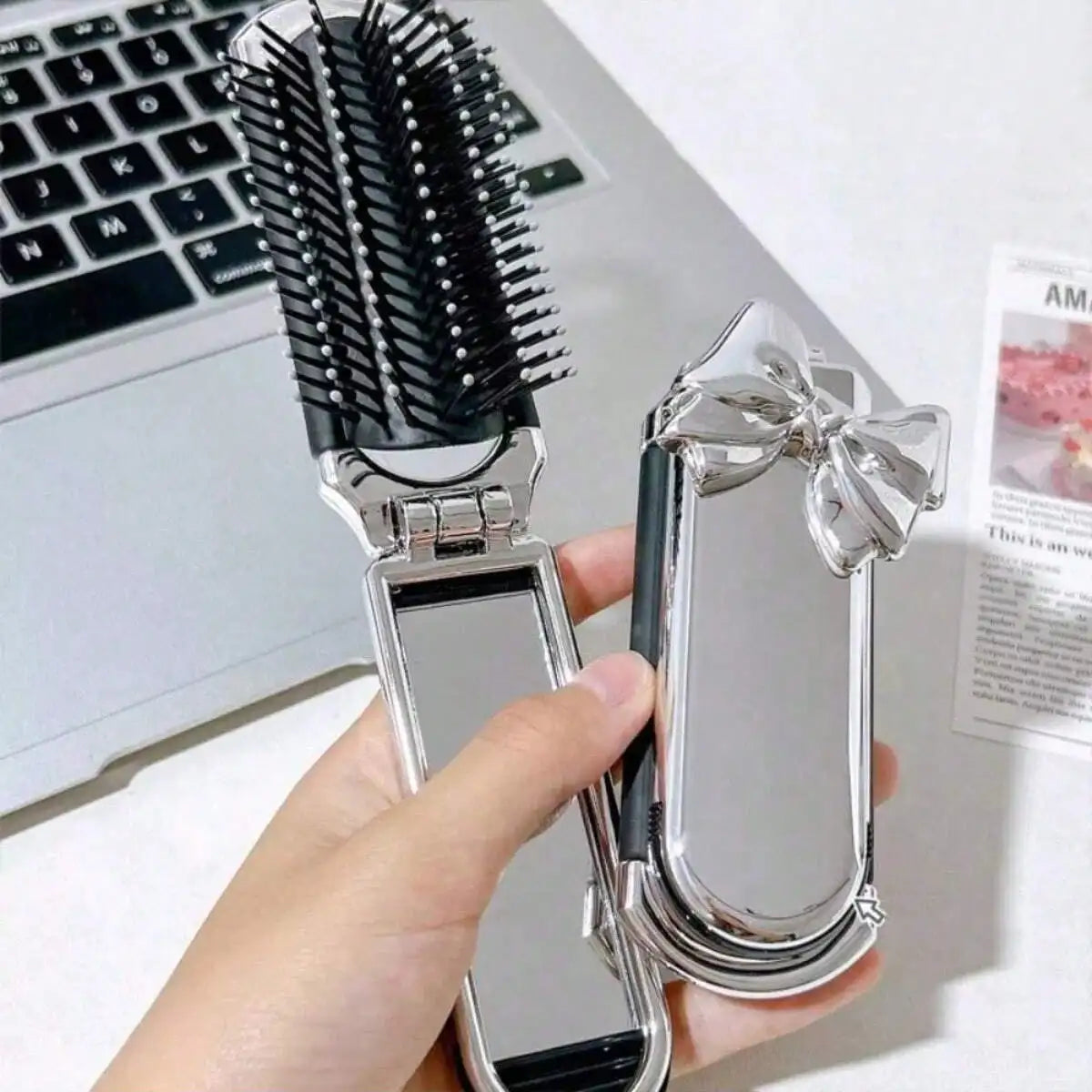 A hand holds a portable compact comb with an airbag and mirror next to a laptop.