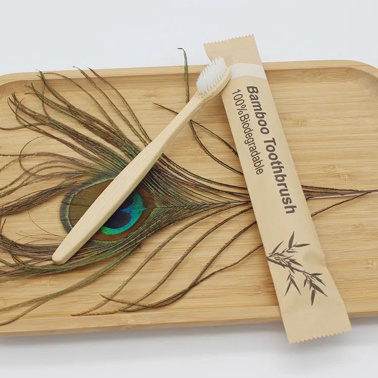 A bamboo toothbrush is shown resting on a wooden board with feathers.