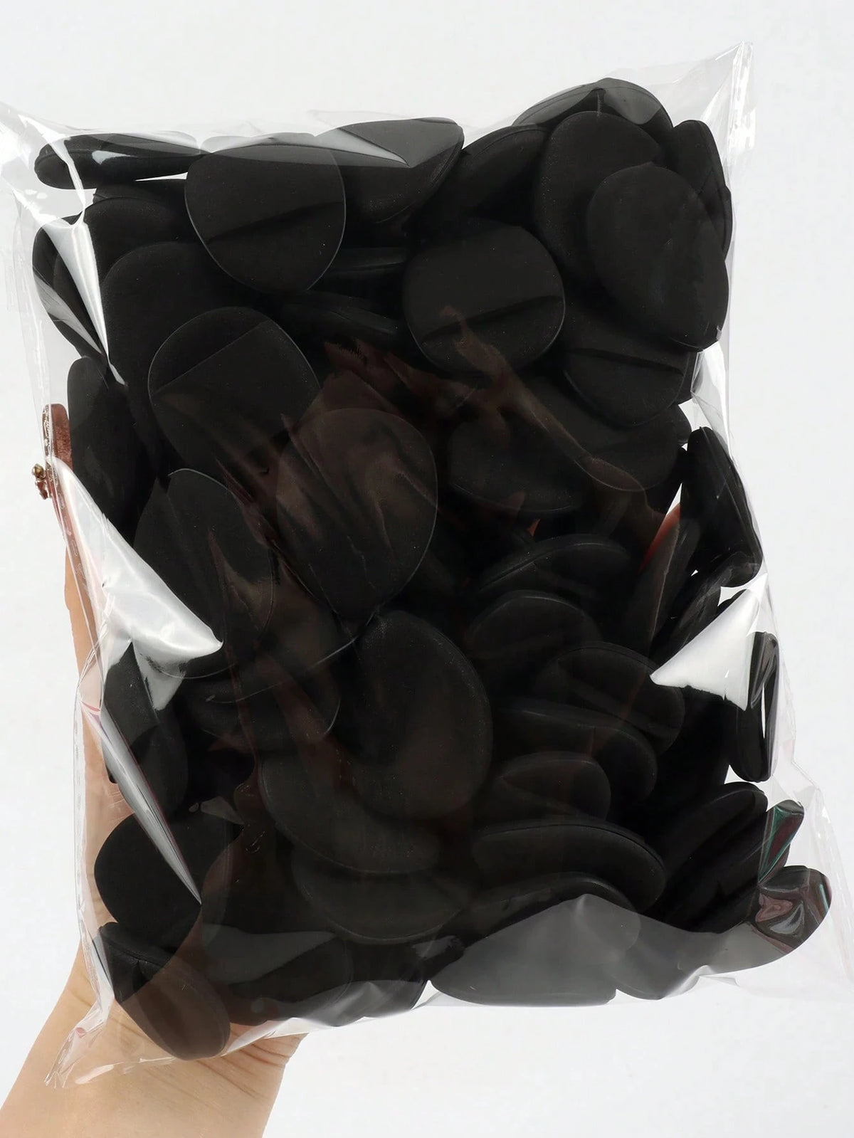 A hand holds a clear plastic bag filled with black latex-free finger puffs for makeup application.