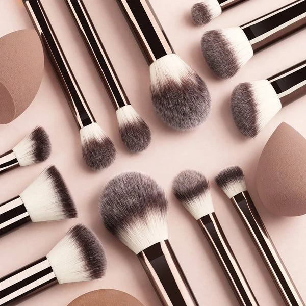 A collection of 12 professional makeup brushes with dark and light gray faux fur bristles arranged on a pink surface.