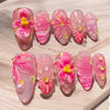 Ein Set rosa und blumiger Press-on-Falschnägel mit irisierenden Finishes und goldenen Akzenten.