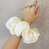 Une main attache une élastique pour cheveux en mousseline de satin blanc autour du poignet.