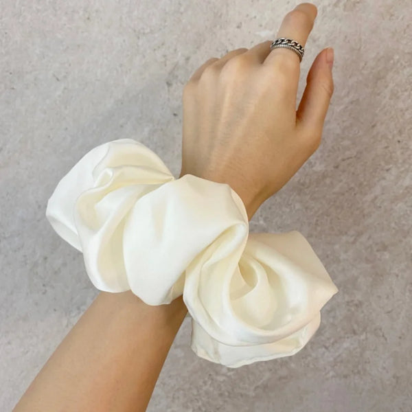 A hand is shown tying a white satin chiffon hair scrunchie around the wrist.