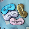 Three embroidered silk sleep masks in blue, gold, and pink are displayed on a light blue background.