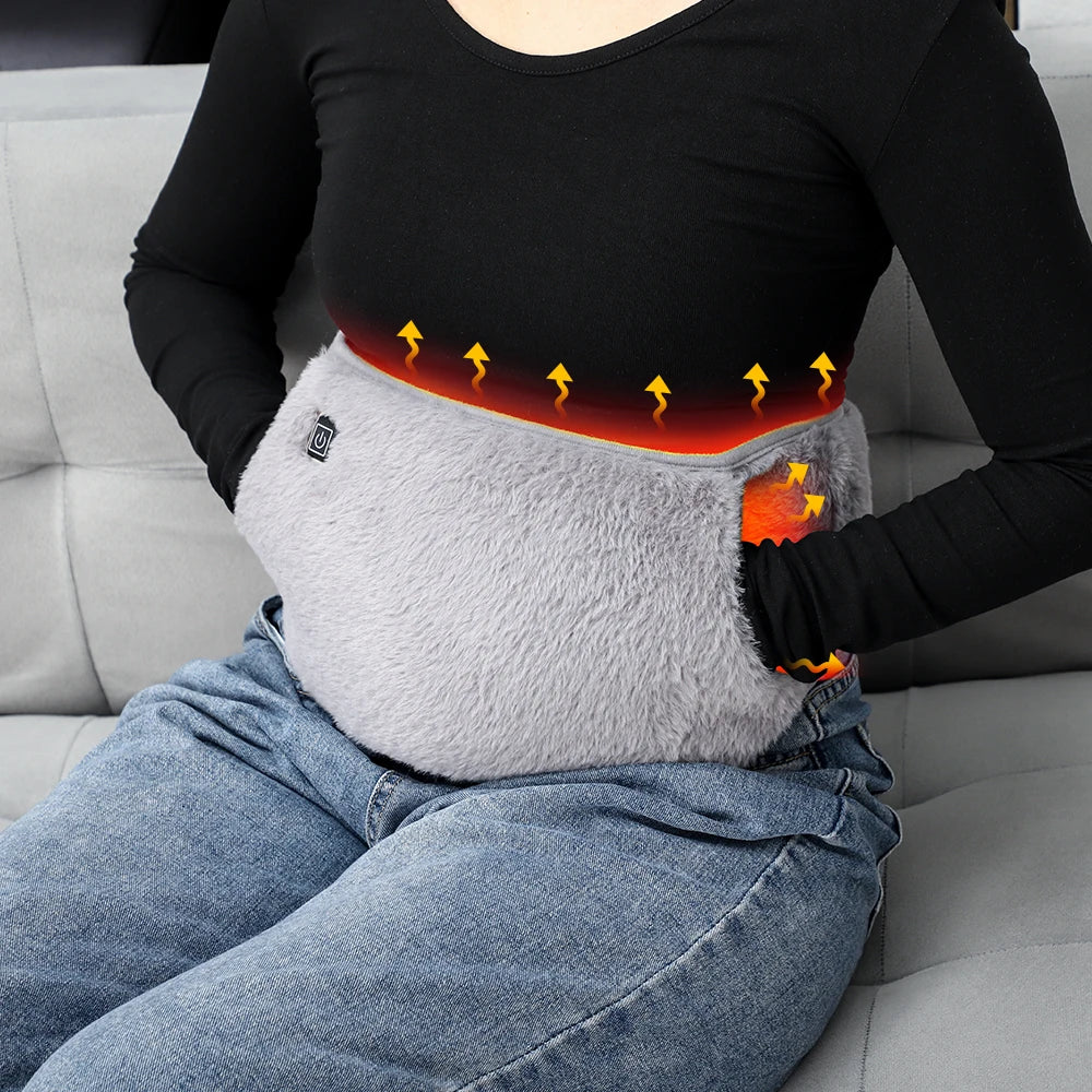 A woman is wearing a gray electric heating therapy belt on her abdomen, with visible heat lines indicating the device's funct