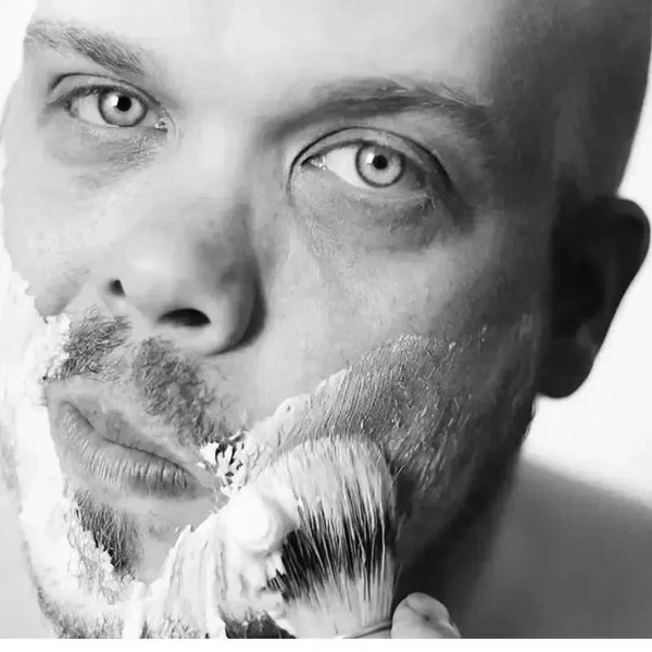 Primer plano en blanco y negro de un hombre afeitándose la barba con un set de cepillo de madera