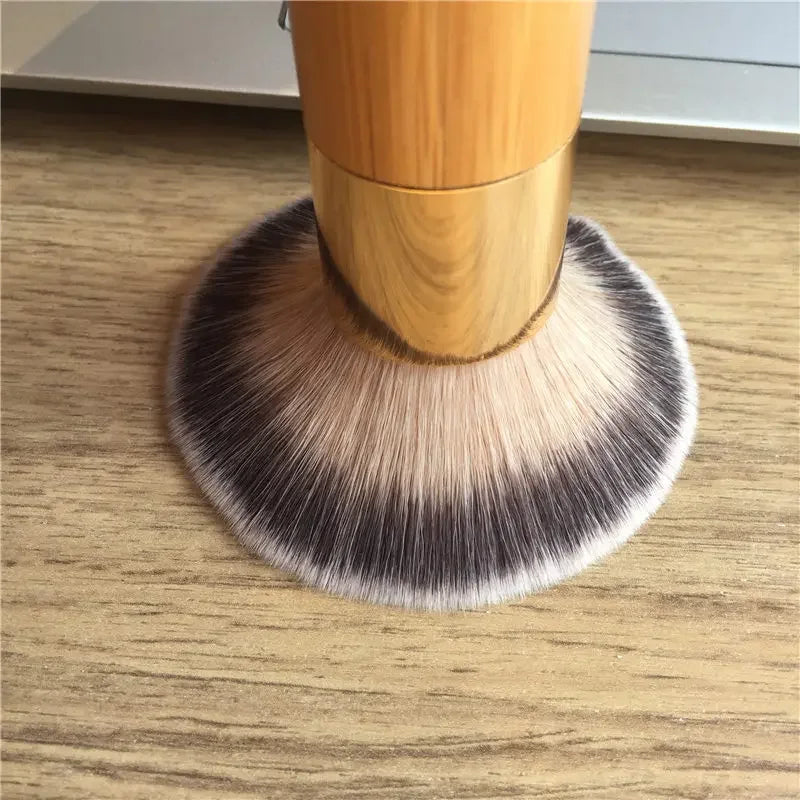 A close-up of a bamboo airbrush foundation and bronzer brush with light brown and black bristles resting on a wooden surface.