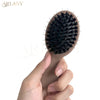 A hand holds a matte boar bristle hair extension brush set with black bristles against a white background.