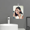 Miroir de vanité en acrylique sans buée avec crochet mural, fixé sur un mur gris au-dessus d'un lavabo blanc.
