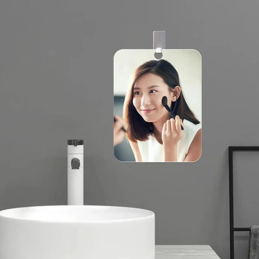 Miroir de vanité en acrylique sans buée avec crochet mural, fixé sur un mur gris au-dessus d'un lavabo blanc.