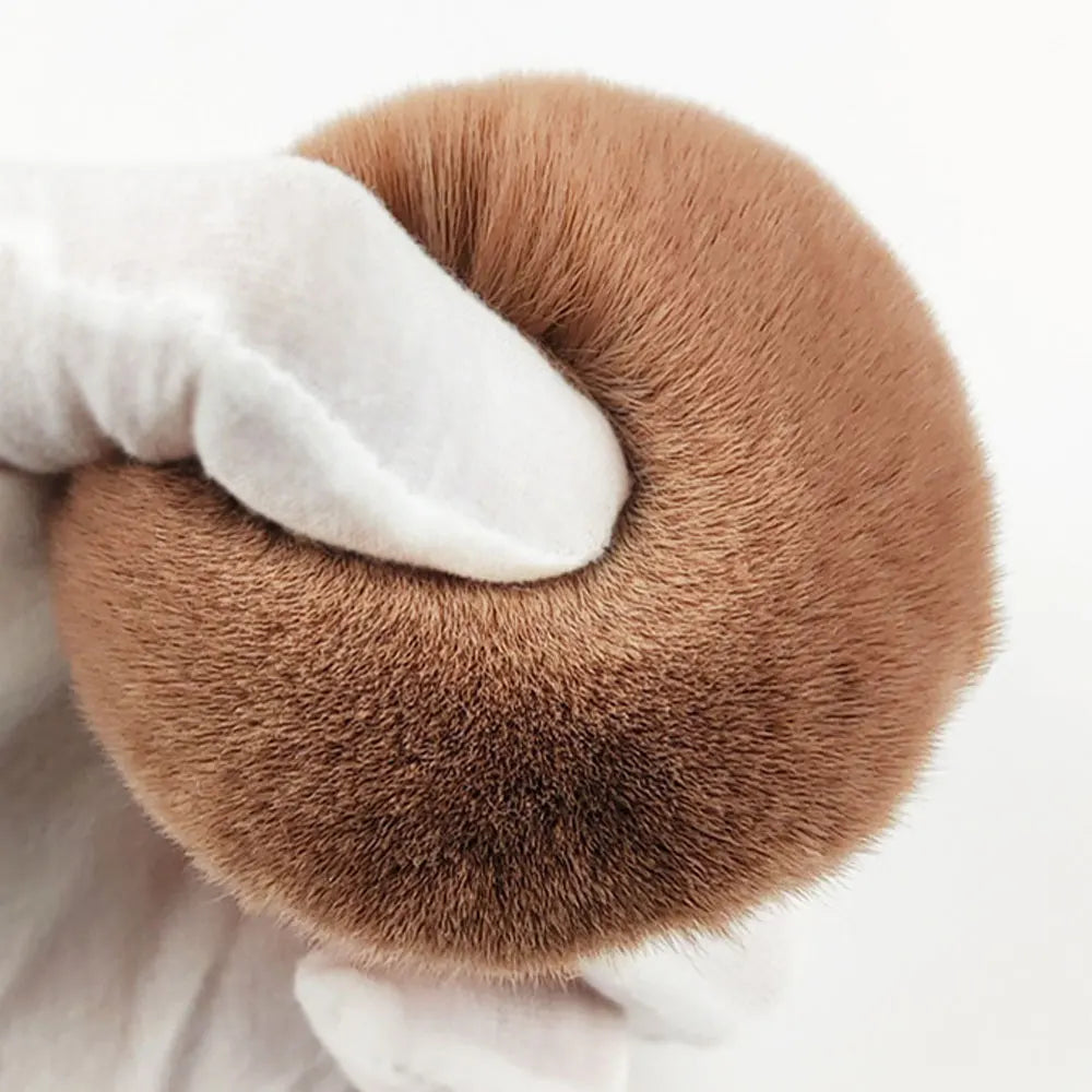 Une main tient une grande brosse de maquillage ronde et marron.