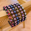 A black rhinestone wave headband featuring colorful floral embellishments displayed on a wooden surface.