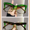 A pair of green patterned reading glasses shown on a hand.
