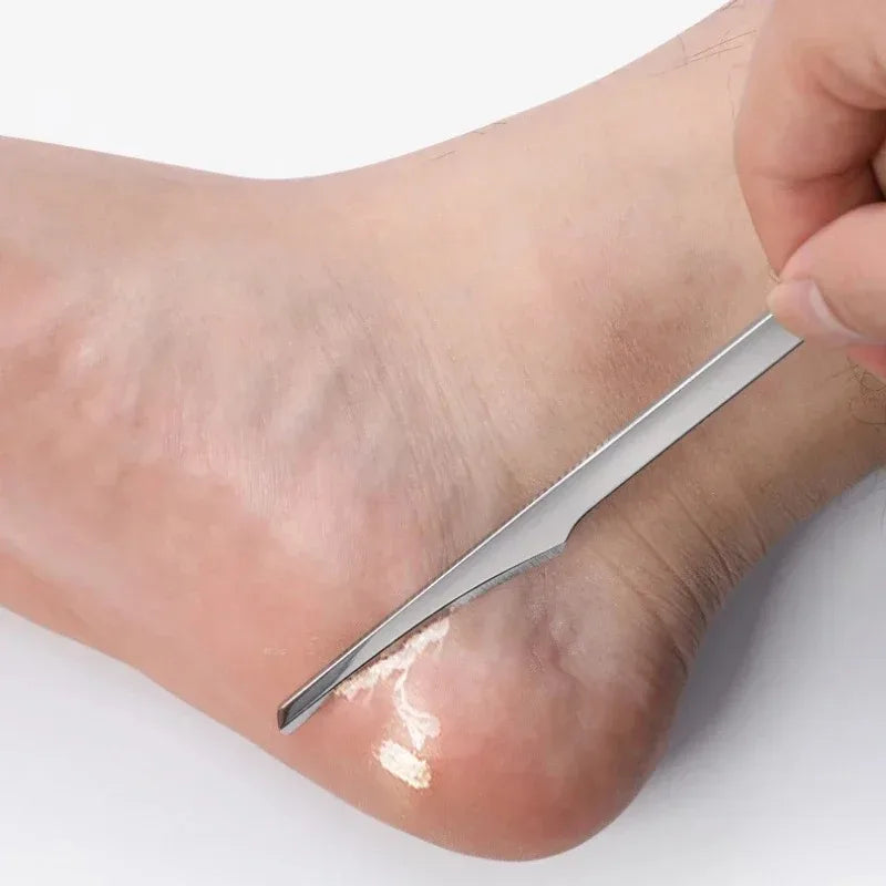 A hand is using a silver multi-piece foot care tool kit to remove dead skin from the sole of a foot.