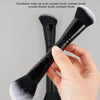 Une main tient un pinceau de maquillage noir à double extrémité avec des poils blancs et noirs sur un fond gris.