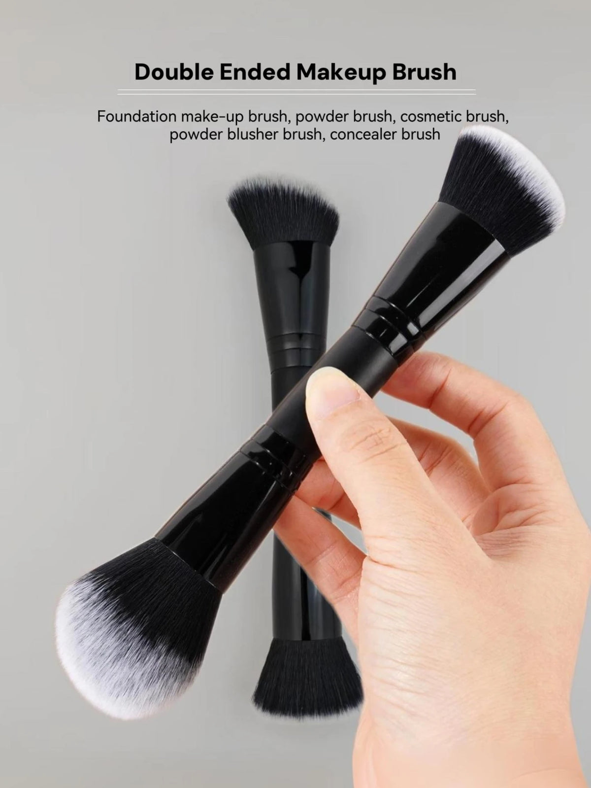 Une main tient un pinceau de maquillage noir à double extrémité avec des poils blancs et noirs sur un fond gris.