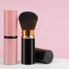 Un set de pinceaux de maquillage rétractables rose et or avec un manche noir et une tête de pinceau, exposé sur une surface b