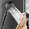 A woman is using a black high-pressure handheld shower head to rinse her face.