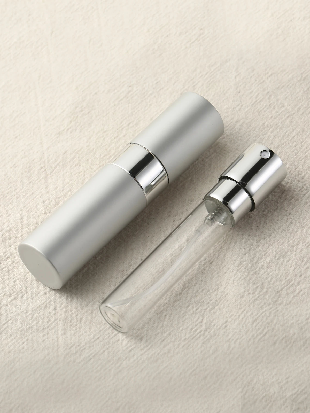 Un set d'atomiseur de parfum argenté avec une bouteille en verre sur un fond de tissu beige clair.