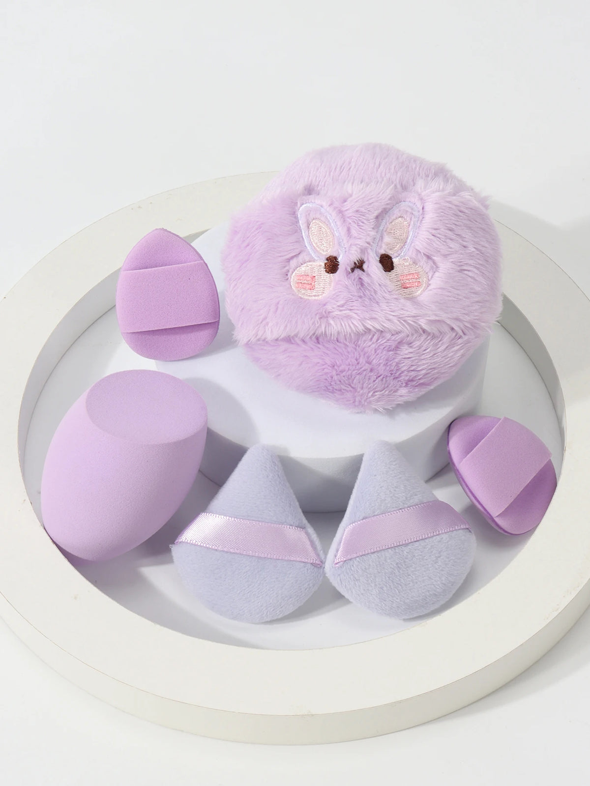 Un ensemble de puffs de poudre brodés en tons lavande et lilas présentés sur une assiette blanche.
