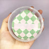 A pink and green checkered makeup puff set is shown inside a clear plastic storage box being held by a hand.