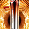 Masajeador facial metálico con luz iluminada sobre un fondo dorado radial brillante.