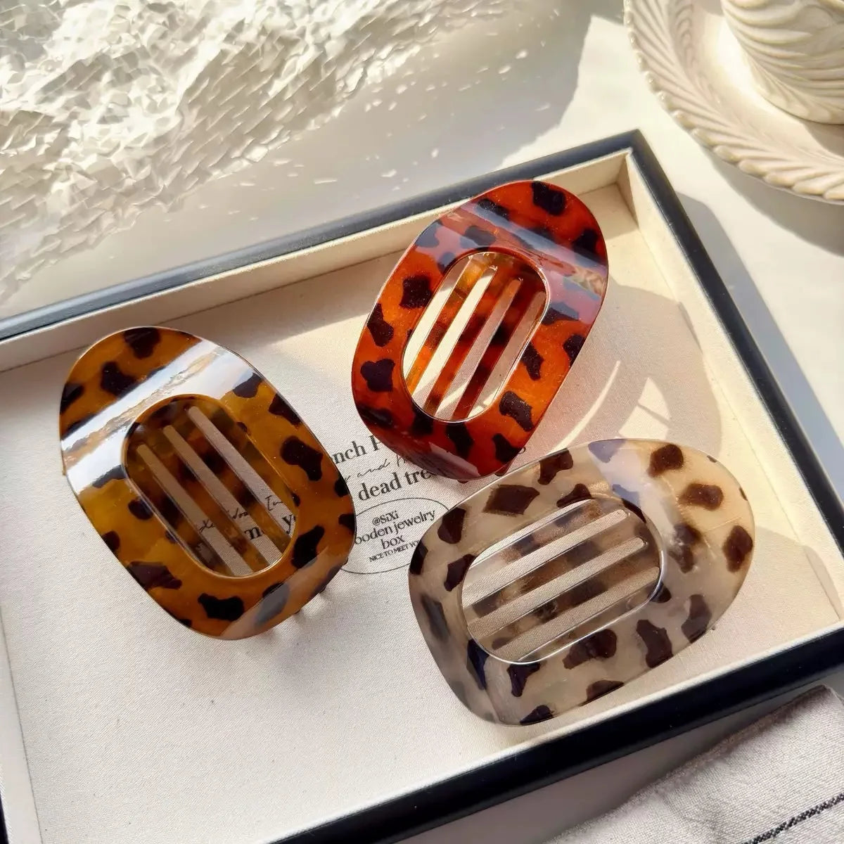 Two oval flat hair clips in leopard print featuring amber and clear acrylic designs displayed in a box.