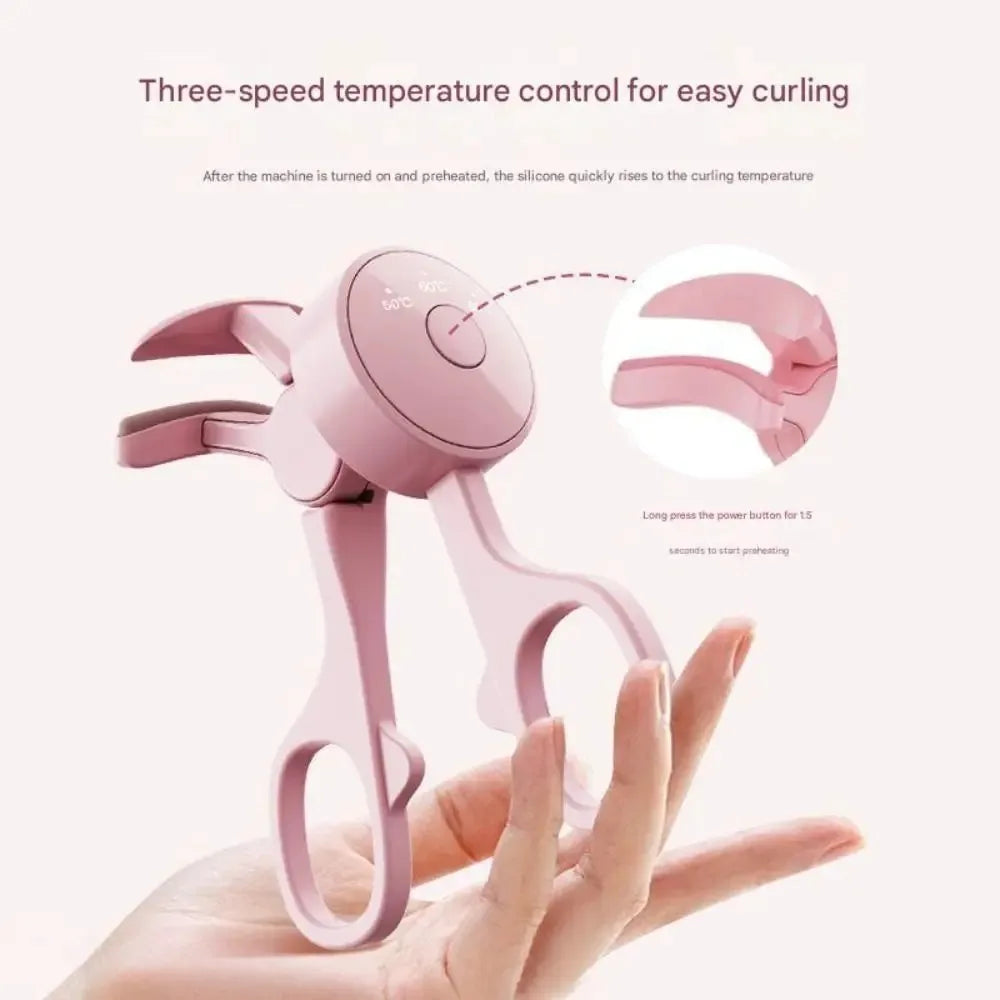 A hand holds a pink frameless heated eyelash curler with temperature control, demonstrating its use.