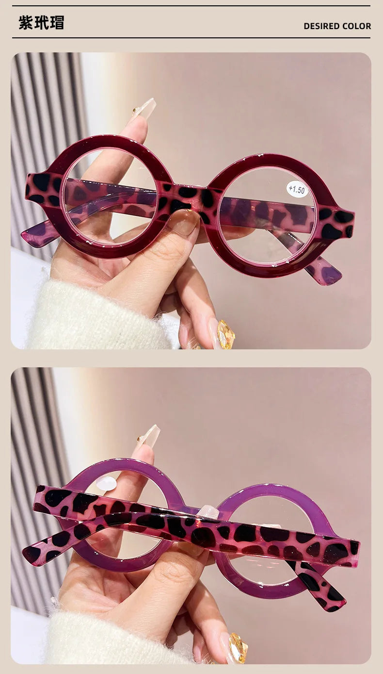 A pair of purple-tinted round acetate reading glasses with a leopard print design being held by a hand.