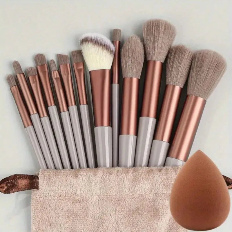 A collection of professional makeup brushes in various shades of rose gold and gray resting on a beige towel.