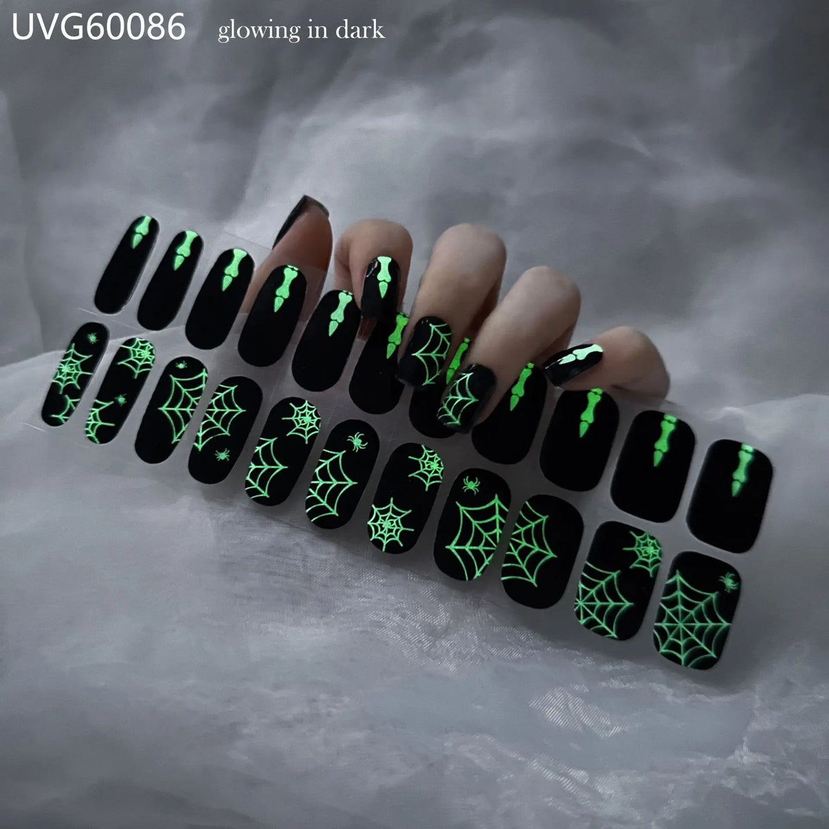 A hand displaying black fingernails decorated with glowing green spiderweb designs for Halloween UV gel nail stickers.