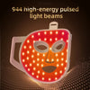 A close-up of an orange LED light therapy face mask emitting bright light beams onto a dark background.