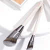 A pair of beige makeup brushes with silver ferrules and fluffy bristles are displayed on a white surface.