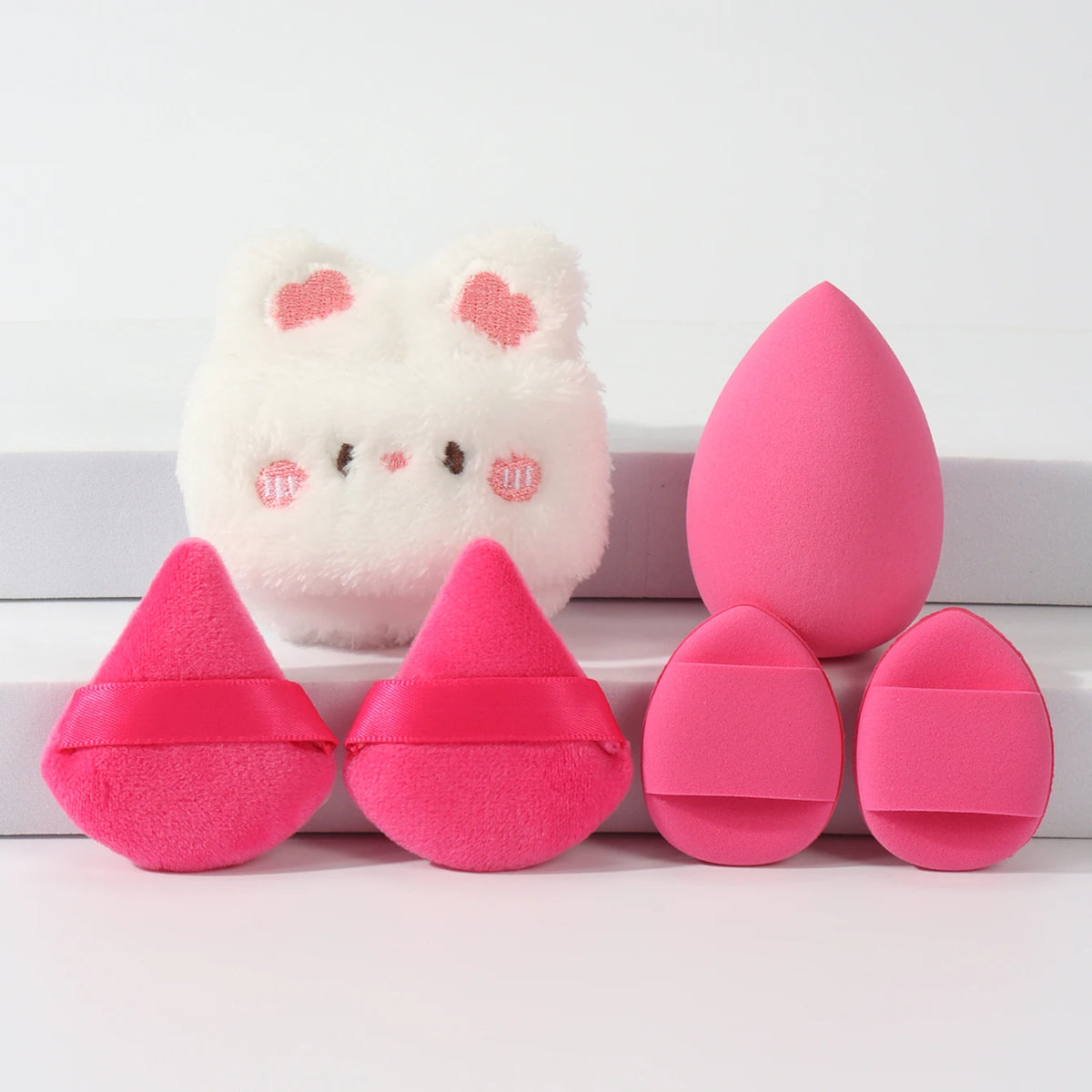 Un ensemble de poudres légères roses et blanches, comprenant une mèche en forme de lapin et plusieurs poudres ovales.