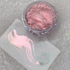 A jar of pink glitter powder next to a white swatch showing a light pink nail art design.