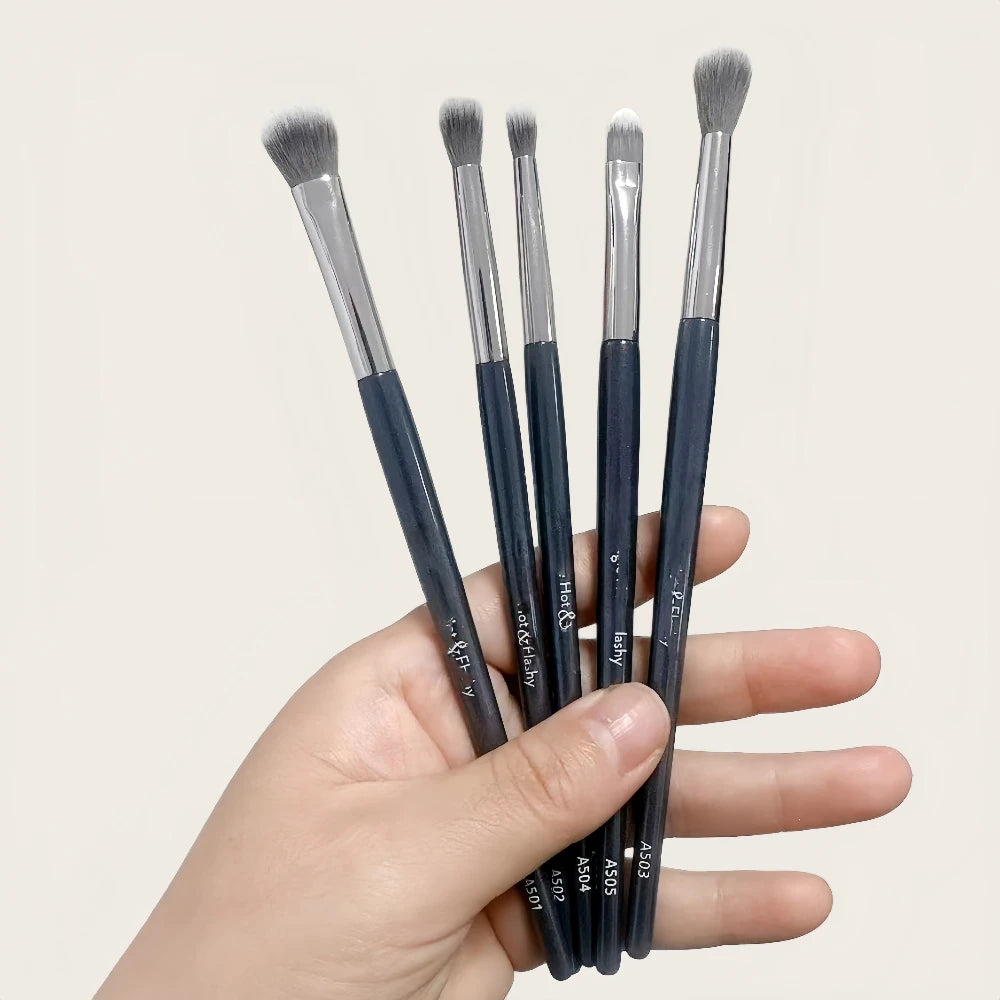 A hand holds several precision concealer brushes for under-eye and contouring in dark blue.
